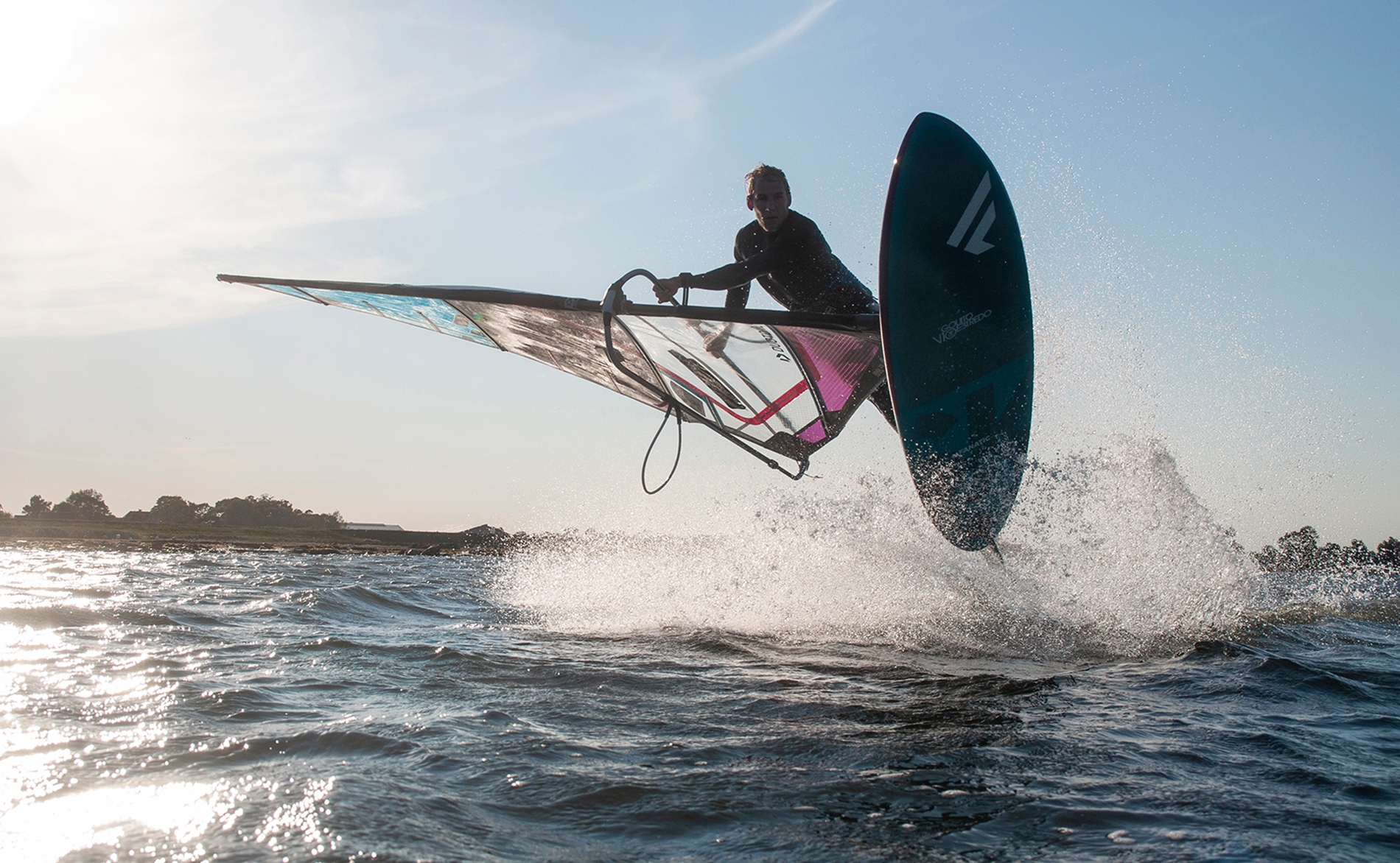 Windsurfen Freestyler Bastian Grimm in Wulfen auf Fehmarn im Flug beim Shaka im Gegenlicht